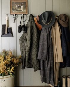 there is a coat rack with hats and coats hanging on the wall next to a potted plant