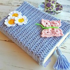 a crocheted book with flowers on it sitting on a table next to a cup and saucer