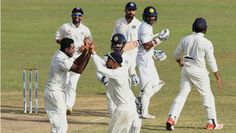 a group of men standing on top of a field playing a game of cricket in white uniforms