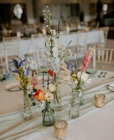 several vases with flowers are sitting on a table in front of white linens