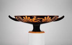 an orange and black bowl sitting on top of a white pedestal