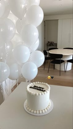 a white cake sitting on top of a table next to balloons in the shape of letters