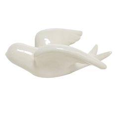 two white ceramic birds sitting next to each other on a white surface with one bird flying towards the camera