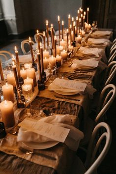 a long table with many lit candles on it and napkins in front of them