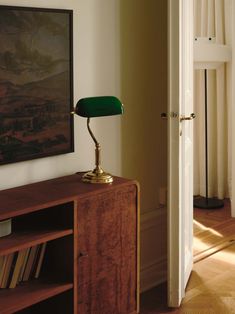 a green lamp sitting on top of a wooden table next to a book shelf and door