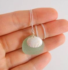 a hand holding a sea glass necklace with a shell charm on it's chain