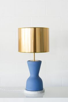 a blue table lamp with a gold shade on the base and a white brick wall behind it