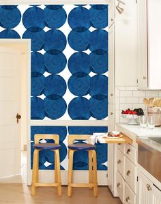 two wooden stools in front of a blue wallpapered kitchen area with white cabinets