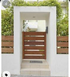 an open wooden gate in front of a white wall with plants and bushes behind it