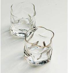 two clear glasses sitting next to each other on a white surface with one empty glass in the middle