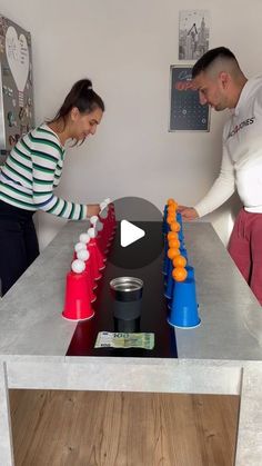 a man and woman playing a game with plastic cups on the table in front of them