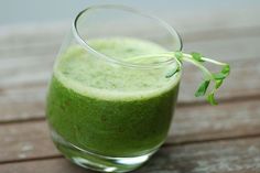 a glass filled with green liquid on top of a wooden table