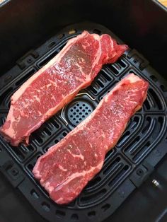 two raw steaks are being cooked in an air fryer with grates on the side