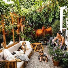 a woman sitting on a couch next to a dog in a garden with potted plants