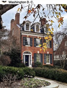 a large brick house with black shutters on the front and side windows, surrounded by greenery