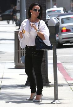 a woman standing next to a parking meter and holding a cell phone in her hand