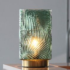 a green glass lamp sitting on top of a wooden table next to a white wall