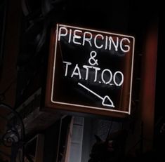 a sign that says piercing and tattoo on the side of a building at night time