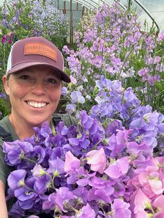 a woman is smiling and holding a bunch of purple flowers in a garden center filled with lots of green plants