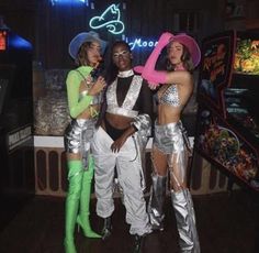 three women dressed up in disco outfits and hats posing for the camera with neon lights behind them