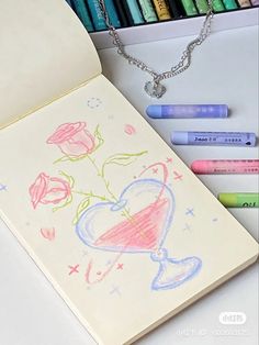 some crayons are next to an open notebook with a drawing on it and a rose