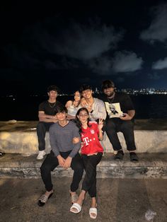 four people posing for the camera at night with their arms around each other and one person holding an open book