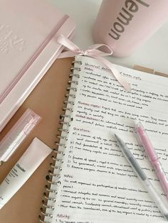 a pink notebook with some writing on it next to a pen and a cup filled with liquid