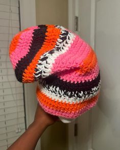 a hand holding up a knitted hat in front of a door