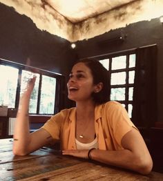 a woman sitting at a wooden table with her hand up in the air and smiling