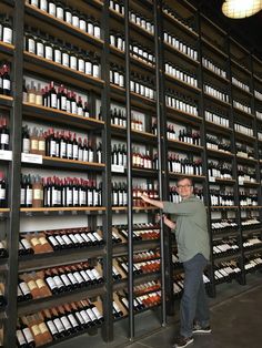 a man standing in front of a wall full of wine bottles and shelves filled with wines