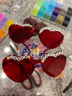 red heart shaped sunglasses with words written on them sitting on a counter next to beads and scissors