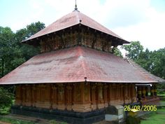 an old wooden building with a red roof in the middle of some grass and trees