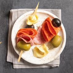 a white plate topped with meat and veggies on top of a cloth next to olives