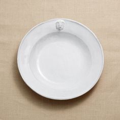 a white bowl with a flower on the side sitting on a beige surface next to a wall