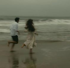 two people running on the beach in front of the ocean