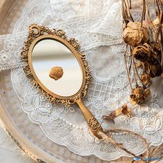 an antique mirror sitting on top of a lace covered table cloth next to dried flowers