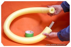 a person is holding a yellow tube and some tape on an orange surface with a white object in the middle