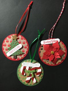 three christmas ornament hanging from red and green ribbons on a black table top