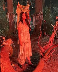 a woman standing in the middle of a forest with red lights on her head and dress