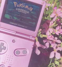 a pink game boy advance sitting next to some flowers