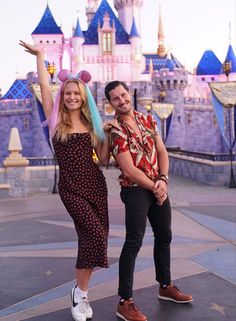 a man and woman posing in front of the castle at disneyland world with their arms up