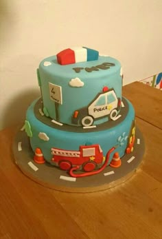 a three tiered cake with cars and trucks on it sitting on top of a wooden table