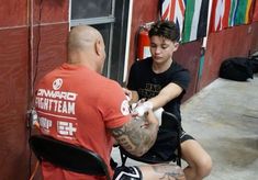 a young man getting his arm tattooed by an older man in a red t - shirt