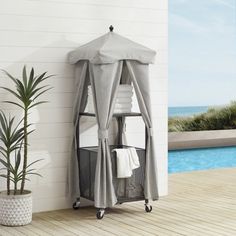 an outdoor shower is next to a pool with a towel rack on wheels and a potted plant