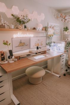 a desk with two computer screens on it and some plants in the corner next to it