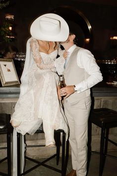 a man and woman dressed in wedding attire kissing each other while sitting at a bar