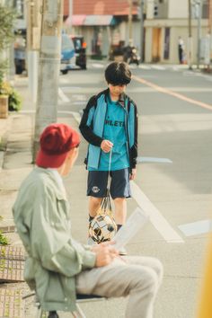 a man sitting on a bench with a soccer ball in his hand and another person standing next to him