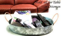 a metal tray with remotes and other items in it sitting on a table next to a couch