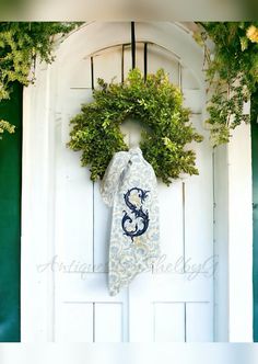 a white door with a wreath on it and a blue monogrammed tie hanging from the front