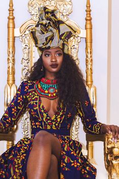 a woman sitting on top of a gold chair wearing a dress and headpieces